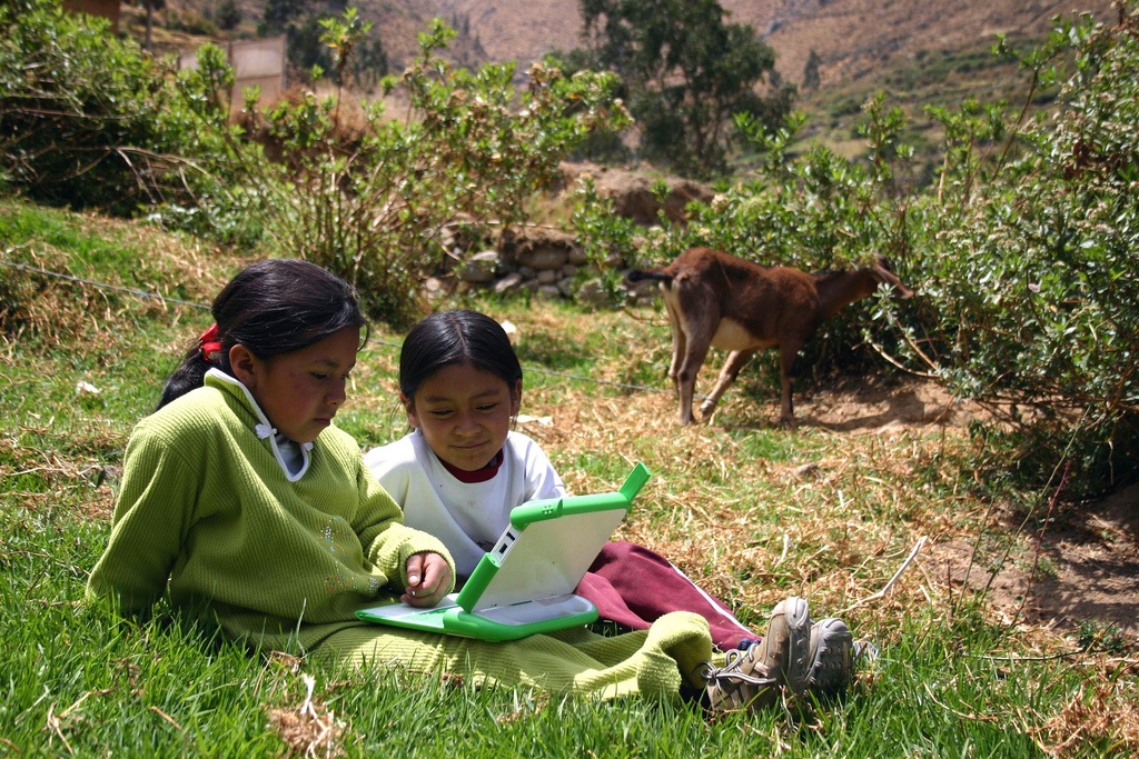 2 Children using an XO in a sunny field in Paraguay with a goat.